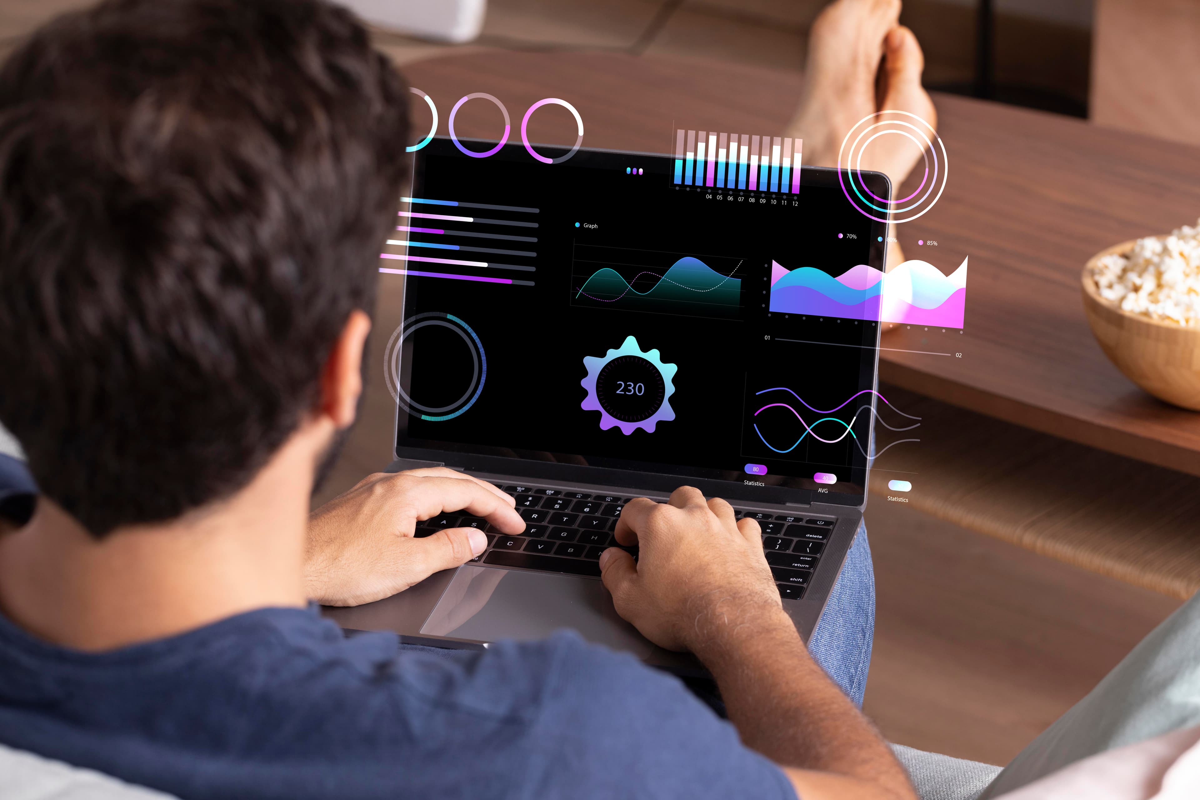 Person working on a laptop displaying a futuristic user interface with various digital charts, graphs, and data visualizations in a relaxed home setting.